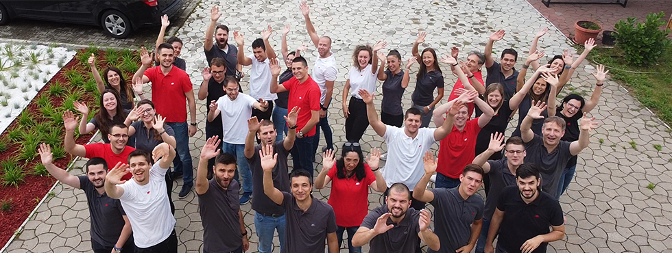 A group of individuals wearing Typhoon HIL shirts, standing together and waving to the drone.