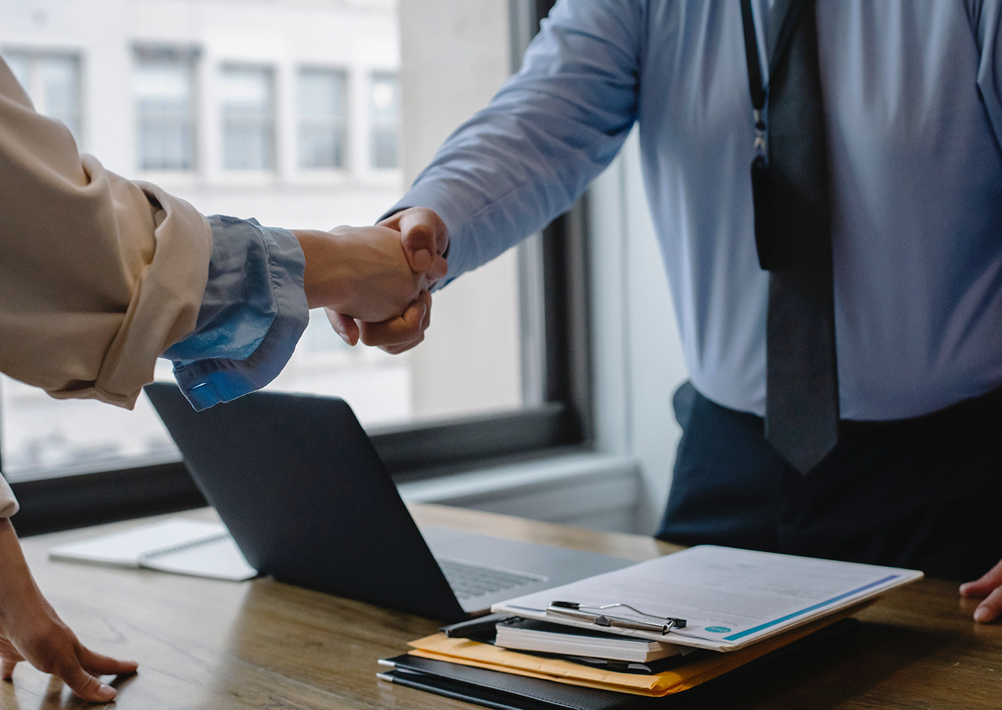 Two individuals shaking hands over a laptop, symbolizing a successful collaboration and partnership.