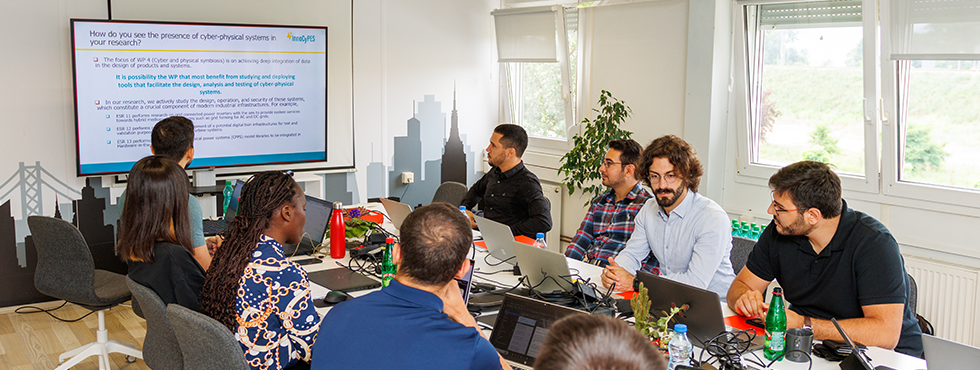 A group of individuals working on laptops at a table, engaged in a collaborative discussion.