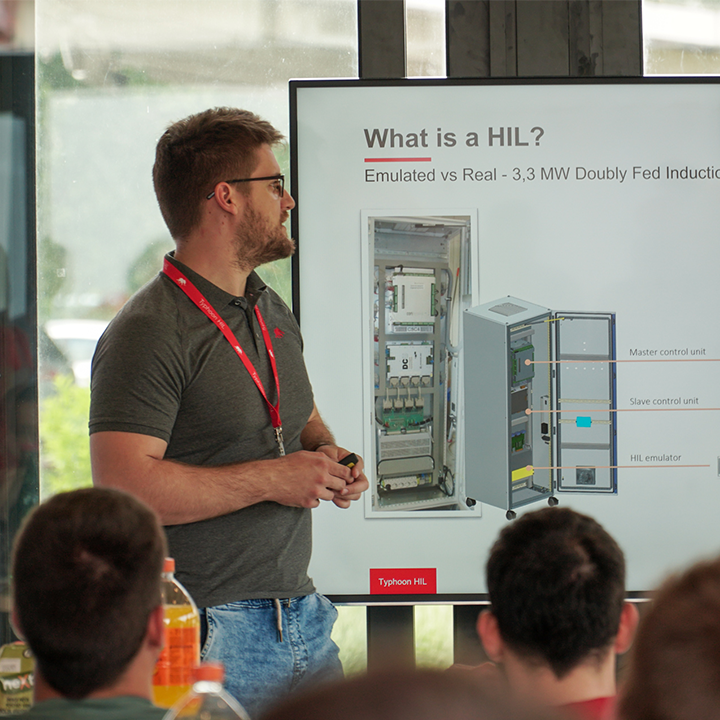 A man confidently presenting in front of an audience, using Typhoon HIL visual aids.