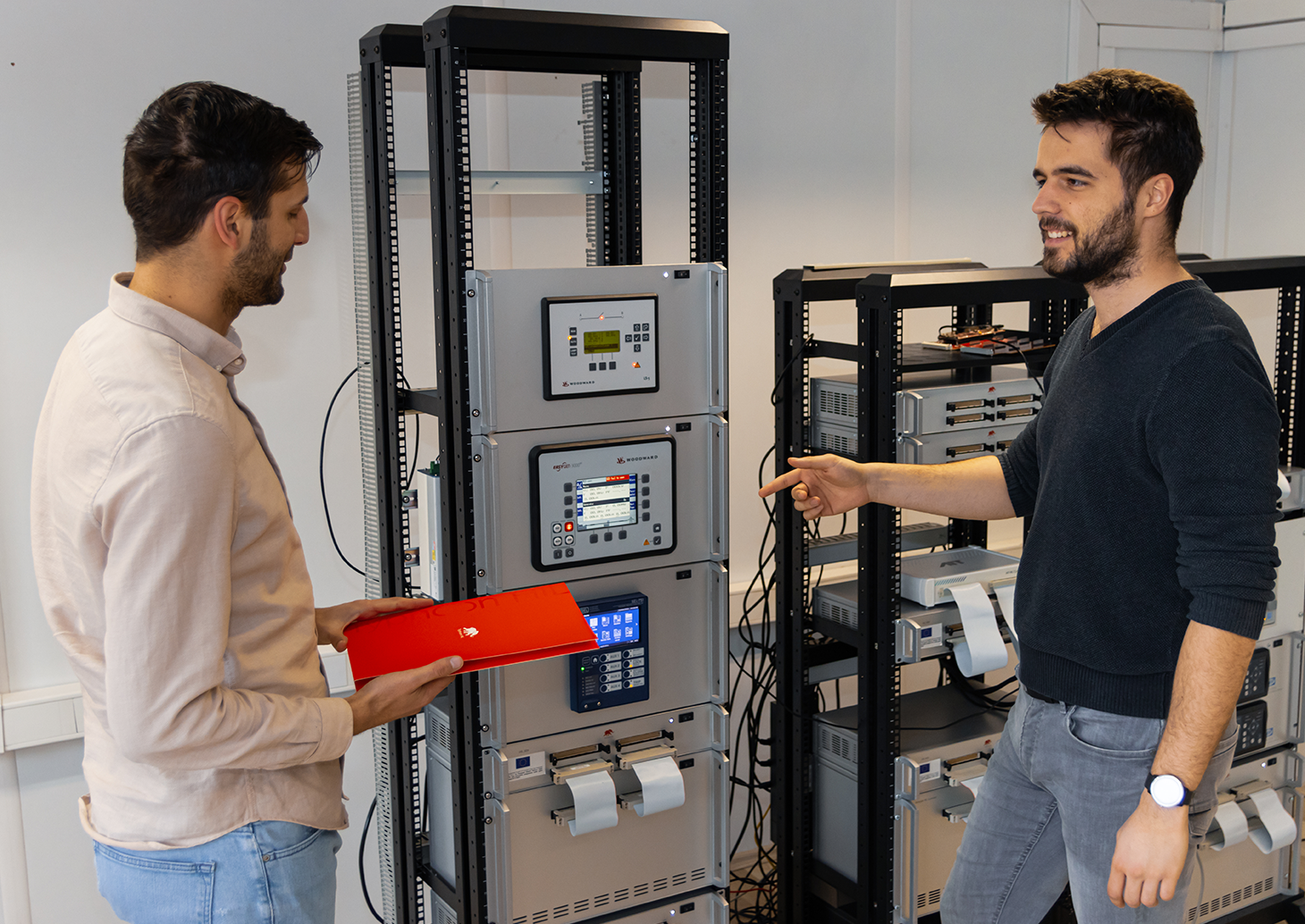 Two men standing in front of a rack of electronics, examining the devices on display.