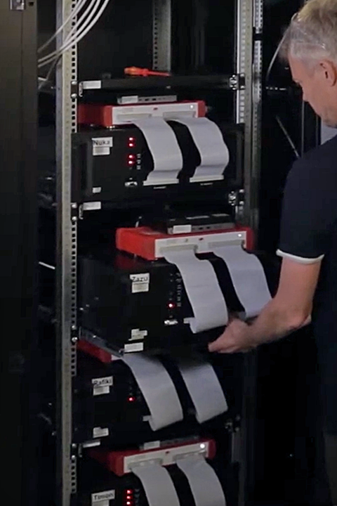 A man observing a row of devices in a rack.