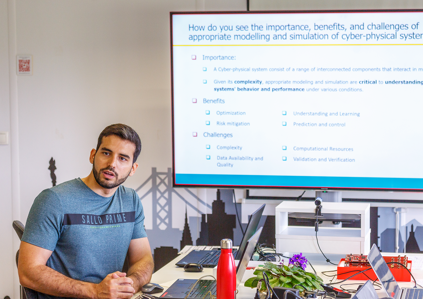 A man sitting in front of a screen and giving a presentation.