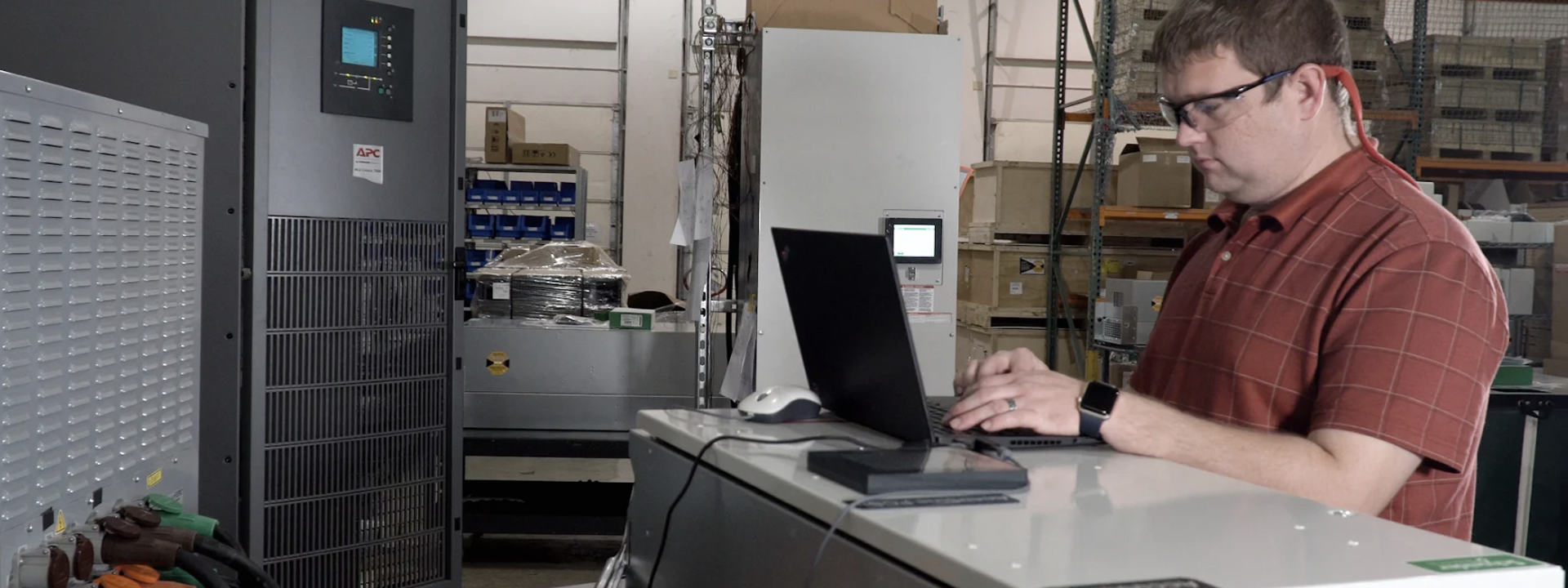 A man working on a laptop amidst the machinery in a factory, focusing on his tasks.